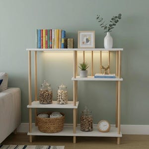 May include: A white and light wood shelving unit with multiple levels, featuring vertical dowel supports. The shelves hold books, a framed print, a white vase with greenery, glass jars filled with nuts, a small potted plant, and a round clock.