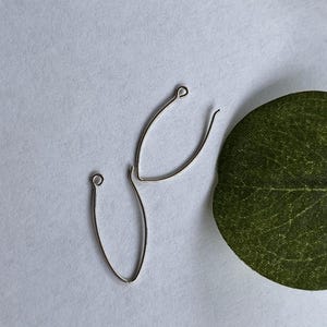 Puede incluir: Dos componentes de pendientes de metal plateado con forma de gotas alargadas y abiertas. Cada pieza presenta un marco de alambre fino y curvado que se estrecha en punta hacia abajo e incluye un pequeño bucle circular en un extremo para sujeción.