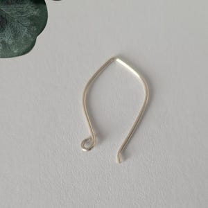 May include: A silver-colored metal earring hook with a pointed, angular top and a curved, teardrop-like shape. One end of the wire features a small, circular loop for attaching jewelry components, while the other end remains open and straight.