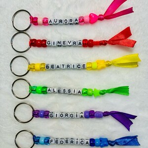 Può includere: Sei portachiavi con anelli in metallo, perline di plastica colorate e cubetti bianchi con lettere che compongono i nomi AURORA, GINEVRA, BEATRICE, ALESSIA, GIORGIA e FEDERICA. Ogni portachiavi termina con un nastro in tessuto abbinato e un ciondolo.