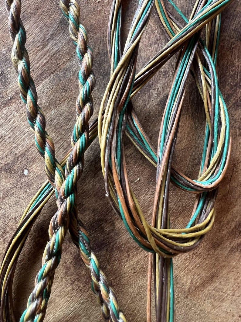 May include: Close-up of braided cords in shades of brown, green, and yellow. The cords are intertwined, creating a textured pattern. The background is a wooden surface.