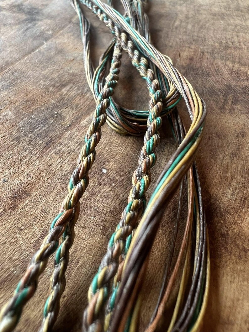May include: Close-up of a collection of braided cords in shades of brown, green, and yellow. The cords are intertwined, creating a textured and layered effect. The image highlights the intricate braiding and the natural color palette of the cords.
