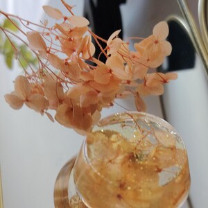 May include: A clear resin sphere containing embedded peach-coloured dried hydrangea petals and gold flakes, accompanied by a matching sprig of dried peach hydrangea flowers extending upwards from the top of the resin piece.