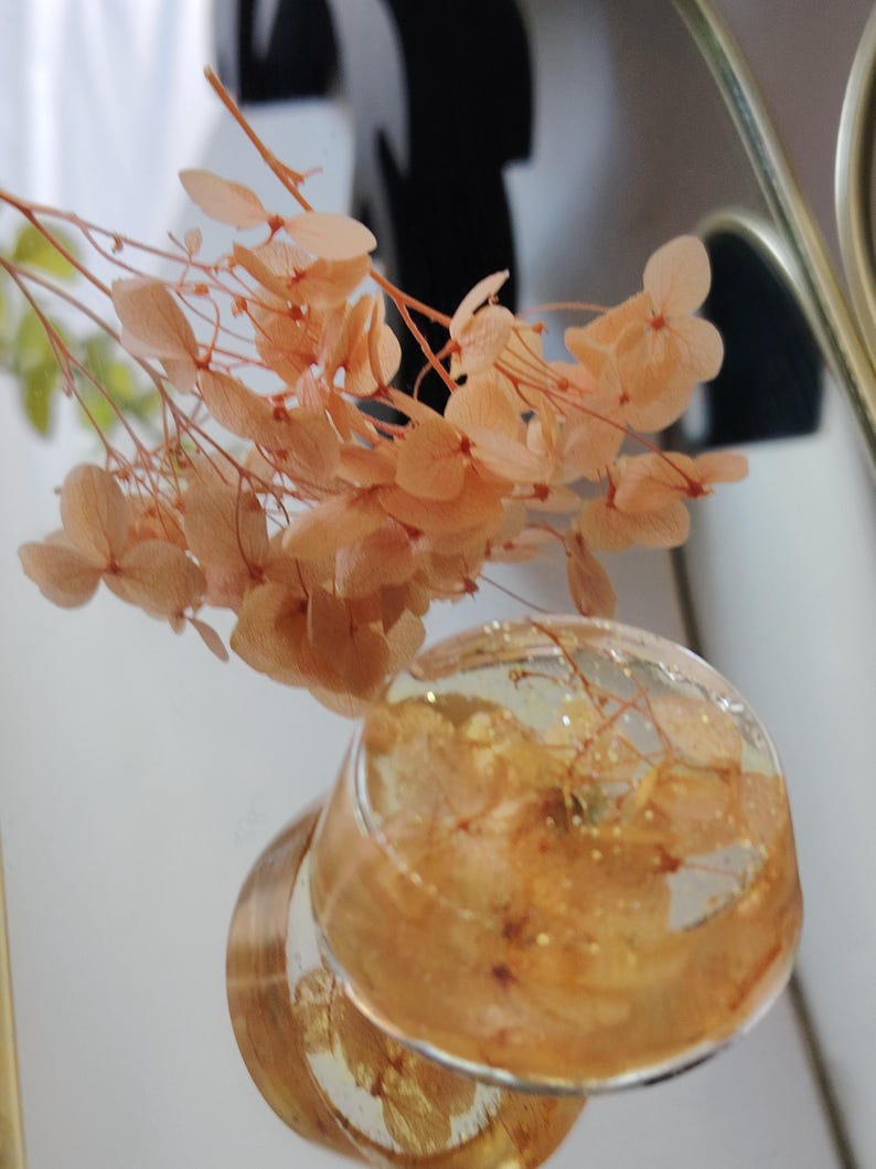 May include: A clear resin sphere containing embedded peach-coloured dried hydrangea petals and gold flakes, accompanied by a matching sprig of dried peach hydrangea flowers extending upwards from the top of the resin piece.