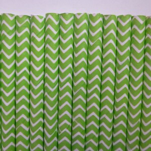 May include: A collection of green and white chevron patterned paper straws. The straws are arranged vertically, creating a visually appealing and decorative element. The bright green color and zig-zag pattern are eye-catching.