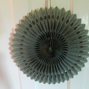 May include: A large, green paper fan with a spiral design and cut-out details. The fan is made of multiple layers of paper and is hanging from a ceiling or wall.