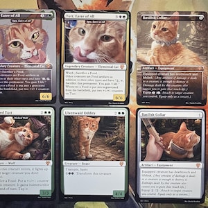 May include: Six rectangular trading cards featuring orange tabby cats. The cards include text such as Tutt, Eater of All, Basilisk Collar, Wicked Tuff, and Ulvenwald Oddity. Each card displays game statistics, ability descriptions, and cat illustrations.