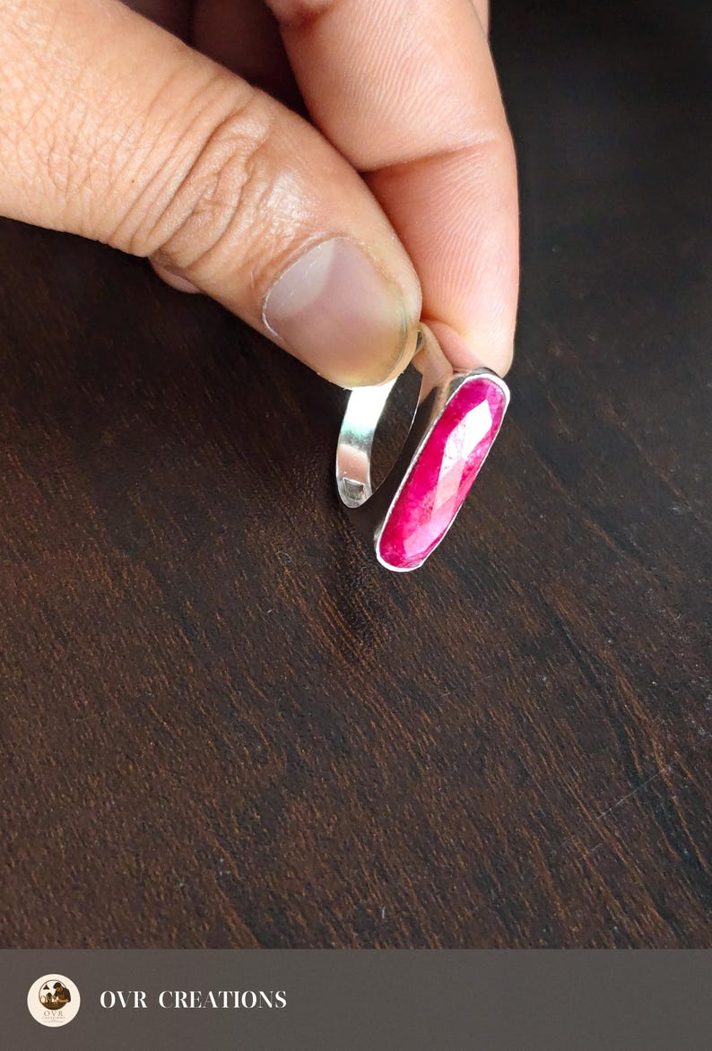 May include: A silver ring featuring a long, narrow, faceted hot pink gemstone set vertically. The ring has a smooth, polished metal band. The image includes the text OVR CREATIONS in the bottom left corner with a small circular logo.