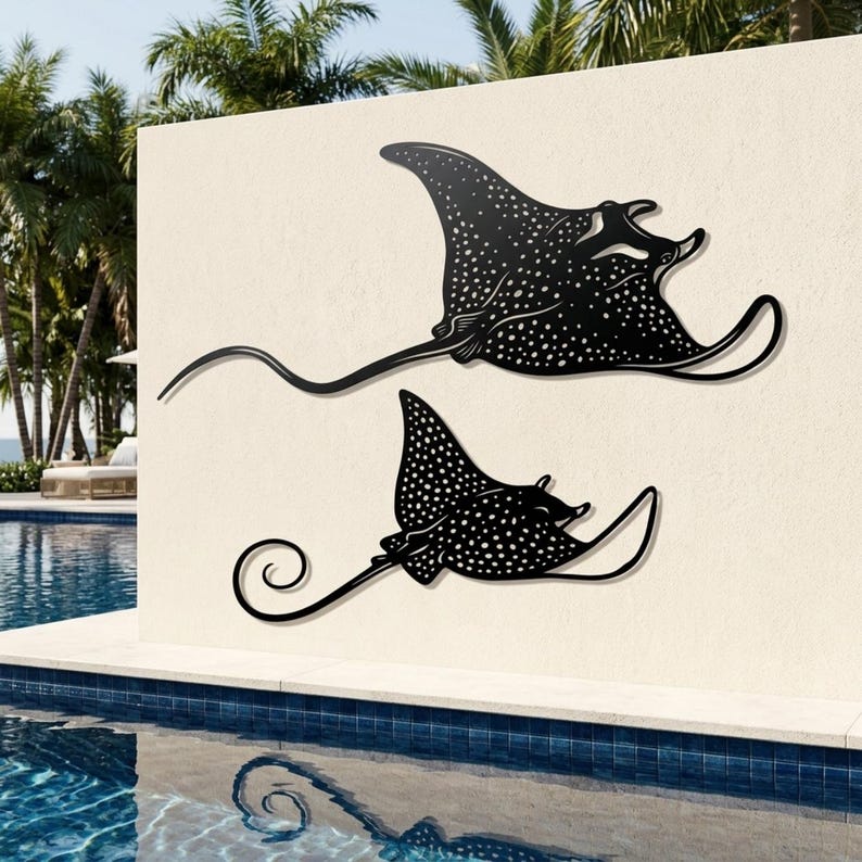 May include: Two black metal wall art pieces shaped like spotted eagle rays. Each ray features a flat silhouette with a long, slender tail and a distinct pattern of white dots across its body. The larger ray is positioned above the smaller one.