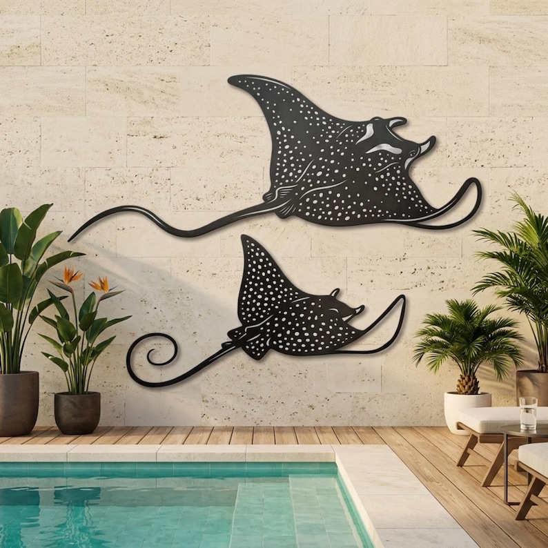 May include: Two black metal wall art pieces shaped like spotted eagle rays. Each ray features a flat silhouette with intricate white dot patterns across the body, wide fins, and a long, slender, curved tail extending from the main body.