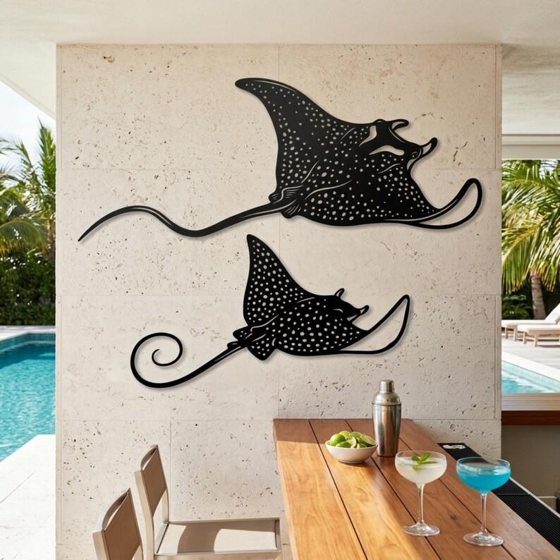 May include: Two black metal wall art pieces shaped like spotted eagle rays. Each ray features a flat silhouette with intricate cut-out white spots across the body, wide fins, and a long, slender tail. The larger ray is positioned above the smaller one.