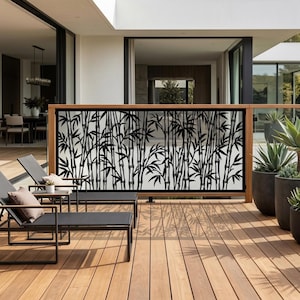 May include: A rectangular metal privacy screen featuring a black laser-cut bamboo stalk and leaf pattern. The screen is framed in wood and installed as a railing on a wooden deck, positioned behind two black lounge chairs with gray cushions.