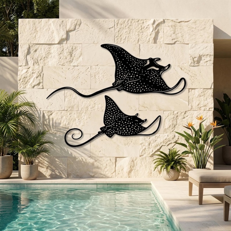 May include: Two black metal wall art pieces shaped like spotted eagle rays, featuring intricate white dot patterns across their bodies and long, slender, curved tails. These flat, silhouette-style marine animal decorations are mounted on a stone wall.