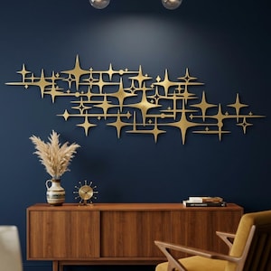 May include: A large, horizontal gold-colored metal wall sculpture featuring an interconnected pattern of multi-pointed stars and thin lines. The piece is mounted on a solid dark blue wall, creating a high-contrast display of geometric shapes.