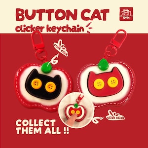 May include: Two apple-shaped clicker keychains with red, white, and green details. One features a black cat face with yellow button eyes, the other a red cat face with yellow button eyes. Both have red clips and text reading BUTTON CAT.