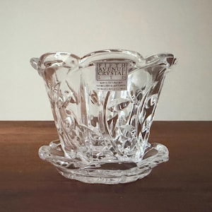 May include: A clear glass planter with a scalloped rim and a matching saucer base. The exterior features a molded floral pattern. A rectangular sticker on the front reads FIFTH AVENUE CRYSTAL LTD, MADE IN CZECH REPUBLIC, FAIT EN LA REPUBLIQUE TCHEQUE.