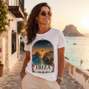 Może przedstawiać: Biały t-shirt z krótkim rękawem z grafiką przedstawiającą nadmorski krajobraz z całkowitym zaćmieniem słońca nad morzem. Tekst IBIZA oraz TOTAL SOLAR ECLIPSE - AUGUST 12, 2026 jest nadrukowany pod ilustracją wewnątrz ozdobnej ramki.