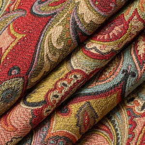 May include: A woven fabric featuring a dense, intricate paisley pattern in shades of deep red, olive green, muted blue, and cream. The material has a visible, textured weave with folded layers that create depth and highlight the complex design.