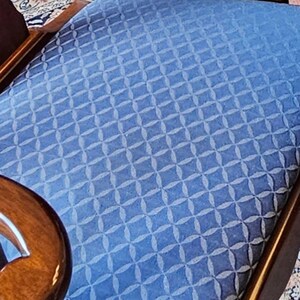 May include: A chair seat upholstered in a blue fabric featuring a repeating geometric pattern of interconnected circles and diamonds. The seat is framed by polished dark brown wooden armrests with curved edges and a smooth, reflective finish.