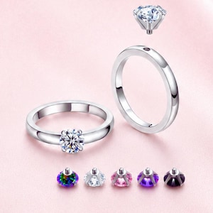 Puede incluir: Un anillo de tono plateado con un engaste desmontable y cinco piedras preciosas intercambiables de corte redondo en colores iridiscente, transparente, rosa, morado y morado oscuro. El anillo tiene un orificio roscado para enroscar la piedra.