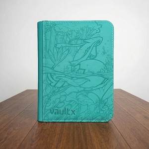 May include: A teal-colored rectangular card binder featuring a textured surface with an embossed forest scene and the text vaultx printed in the bottom left corner. The binder has rounded corners and a vertical stitched seam along the left side.