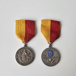 May include: Two circular silver-toned metal medals suspended from yellow and red striped ribbons. The left medal features the text OSTERGOTLANDS BOWLINGFORBUND and a bowling pin emblem. The right medal displays LINKOPINGS BOWLINGKLUBBARS FORENING with a blue shield.