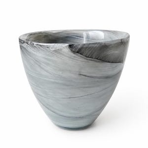 May include: A bowl made of glass featuring a swirling marbled pattern in shades of gray, black, and white. The vessel has a wide, open top that tapers down to a narrow base, with a smooth, polished surface that reflects light across its curved form.