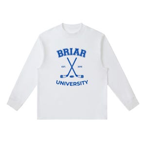 Op de afbeelding: Een wit shirt met lange mouwen en een blauwe grafische print op de borst. Het ontwerp bevat de tekst BRIAR UNIVERSITY in een college-lettertype, twee gekruiste hockeysticks, een puck en de tekst EST. 2015 gecentreerd tussen de sticks.
