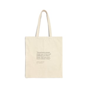 Könnte beinhalten: Eine cremefarbene Stofftasche aus Segeltuch mit zwei Schulterriemen. Auf der Vorderseite befindet sich ein dunkler Text: "Sometimes people sneak up on you and suddenly you don't know how you ever lived without them" gefolgt von "GARRETT GRAHAM - OFF CAMPUS 5".