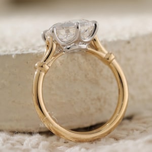 Op de afbeelding: Een ring met een grote, heldere, rondgeslepen edelsteen in een zilverkleurige metalen zetting. De ringband is gemaakt van gepolijst geelgoud en heeft een glad, afgerond profiel dat aansluit op de zilverkleurige zetting van de edelsteen.