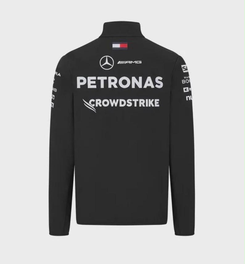 May include: A black long-sleeve jacket featuring a high collar and white printed logos. The back displays the Mercedes-Benz star, AMG, PETRONAS, and CROWDSTRIKE branding, along with a small rectangular Tommy Hilfiger flag logo at the neckline.