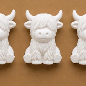 May include: Three identical white figurines shaped like Highland cattle, each featuring a shaggy coat texture, curved horns, and a rounded snout. The figures are arranged in a horizontal row, displaying a consistent matte finish and detailed fur.