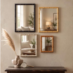 May include: Four rectangular wall mirrors with bamboo-style frames in black, gold, silver, and bronze finishes. The mirrors are arranged in a cluster on a wall. A textured beige vase with a dried plant and a magnifying glass sit on a dark table.
