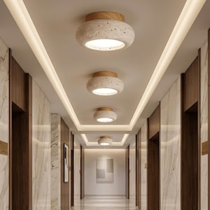 May include: A series of four flush mount ceiling lights arranged in a row. Each light features a circular, porous, beige stone-like shade with a light wood base and a central circular white diffuser that emits a warm, soft glow downwards.