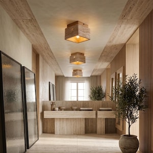 May include: Three square ceiling light fixtures with a textured beige stone finish and a warm glowing bulb inside, mounted in a row along a hallway ceiling. The fixtures feature a natural porous surface and a simple geometric box shape.