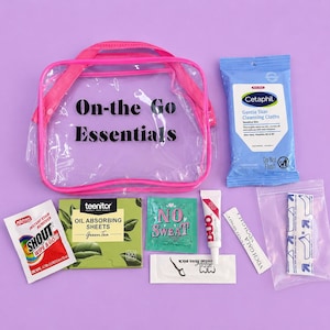 May include: A clear plastic pouch with pink trim and the text On-the Go Essentials, accompanied by a pack of Cetaphil cleansing cloths, Shout stain remover, Teenitor oil absorbing sheets, No Sweat packet, Duo adhesive, a floss pick, and bandages.
