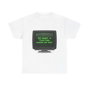 Op de afbeelding: Wit T-shirt met een retro computermonitorafbeelding. De monitor toont de tekst "Git Commit -m 'Fixed bugs, created new ones'" in groene letters. Het T-shirt heeft een ronde hals.