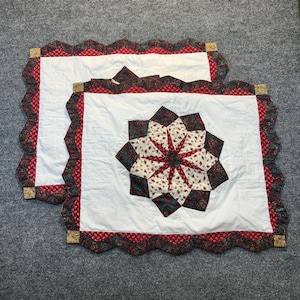 May include: Two square quilted fabric covers featuring a central star pattern in cream, dark green, and red floral prints. The borders are scalloped with a red and green paisley pattern, accented by small tan corner squares on a white background.
