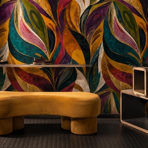May include: A mustard yellow curved bench with rounded legs sits in front of a wall covered in wallpaper featuring a large-scale abstract leaf pattern in shades of teal, deep purple, gold, and white, with two dark brown shoes on a metal shelf.