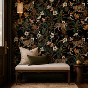 May include: A rectangular bench with a light beige upholstered seat and dark wood legs, featuring a large square beige pillow and a smaller rectangular olive green pillow. The wall behind is covered in black wallpaper with a jungle print.