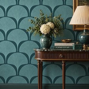May include: A dark teal wallpaper with a repeating fan-shaped pattern in lighter blue. A wooden console table with a marble top holds a green vase with white flowers, a lamp, and two books titled The Kinfolk Home and At Home With Art.
