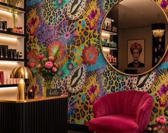 May include: A vibrant interior space featuring a wall with a colorful leopard print and floral pattern, a round gold-framed mirror, a magenta velvet armchair, a black fluted console table with a gold lamp, and a patterned rug on the floor.
