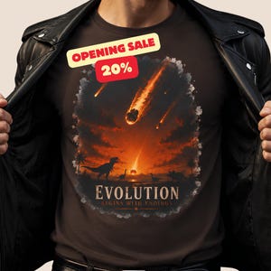 Op de afbeelding: Een donkerbruin t-shirt met een afbeelding van dinosaurussen onder een vurige lucht met vallende meteoren. De tekst luidt "OPENING SALE 20%" en "EVOLUTION BEGINS WITH ENDINGS". Het shirt wordt gedragen onder een zwart leren jack met zilveren drukknopen.