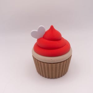 May include: A cupcake-shaped trinket box. The top is red, with a white heart detail. The base is brown with a ribbed design. The frosting is a vibrant red. A decorative item, ideal for small keepsakes.