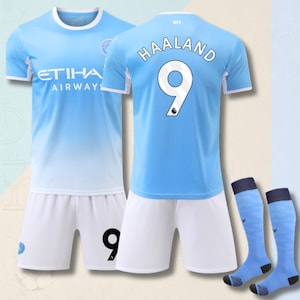 Könnte beinhalten: Ein hellblau-weißes Fußballtrikot-Set bestehend aus einem Trikot mit der Aufschrift ETIHAD AIRWAYS auf der Vorderseite, dem Namen HAALAND und der Nummer 9 auf der Rückseite, passenden weißen Shorts mit der Nummer 9 und hellblauen Fußballstutzen.