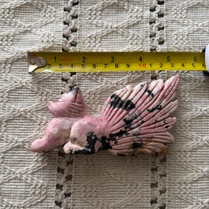 May include: A pink and black carved stone fox figurine with a large, detailed tail. The fox is approximately 5 inches long, measured with a tape measure. The figurine is set on a cream-colored, textured surface.