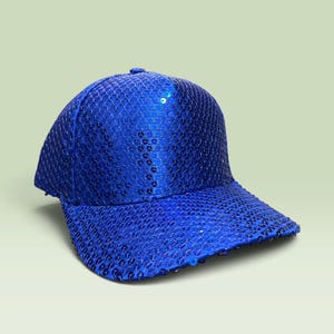 May include: A vibrant royal blue baseball cap completely covered in small, reflective circular sequins. The cap features a structured crown and a curved brim, with the sequins creating a uniform, shimmering texture across the entire surface.