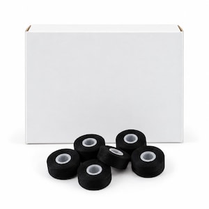 Puede incluir: Una caja rectangular de cartón blanco liso colocada detrás de un grupo de seis pequeñas bobinas circulares de hilo de coser negro. Cada bobina presenta un núcleo de plástico translúcido y está dispuesta en un grupo compacto.