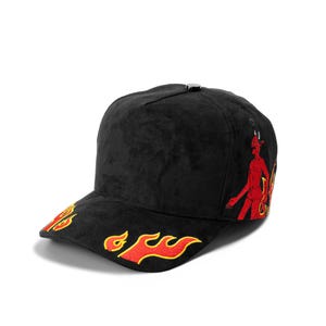 May include: A black baseball cap featuring embroidered red and yellow flame designs on the brim and a red devil figure embroidered on the side panel. The cap has a structured crown with a small black button at the top and a curved visor.