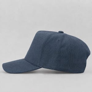 May include: A solid dark blue baseball cap with a structured five-panel crown, a curved brim, and a fabric-covered button at the top centre. The cap features visible stitching along the panels and brim, presenting a clean, uniform appearance.